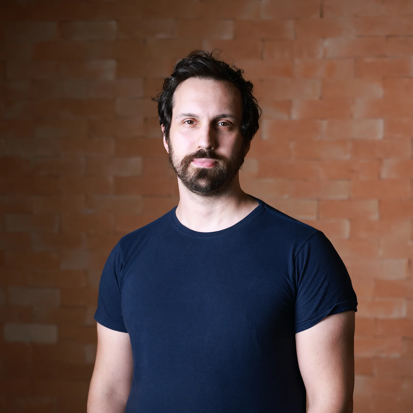 Felipe Fiori, psicanalista, olhando para a câmera diante de uma parede de tijolos, com a mão no bolso.