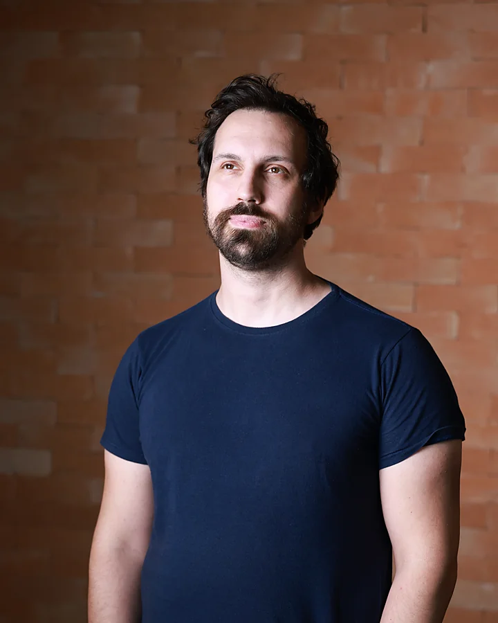 Felipe Fiori, psicanalista, diante de uma parede de tijolos, olhando para cima.